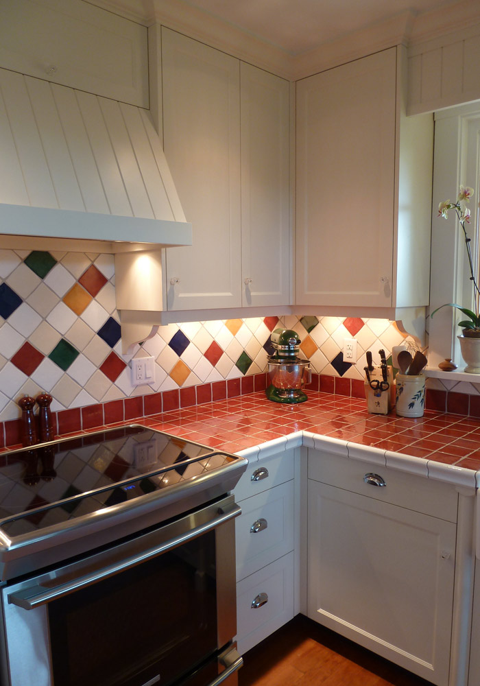 Custom painted range hood above stove with colourful diamond tile backsplash