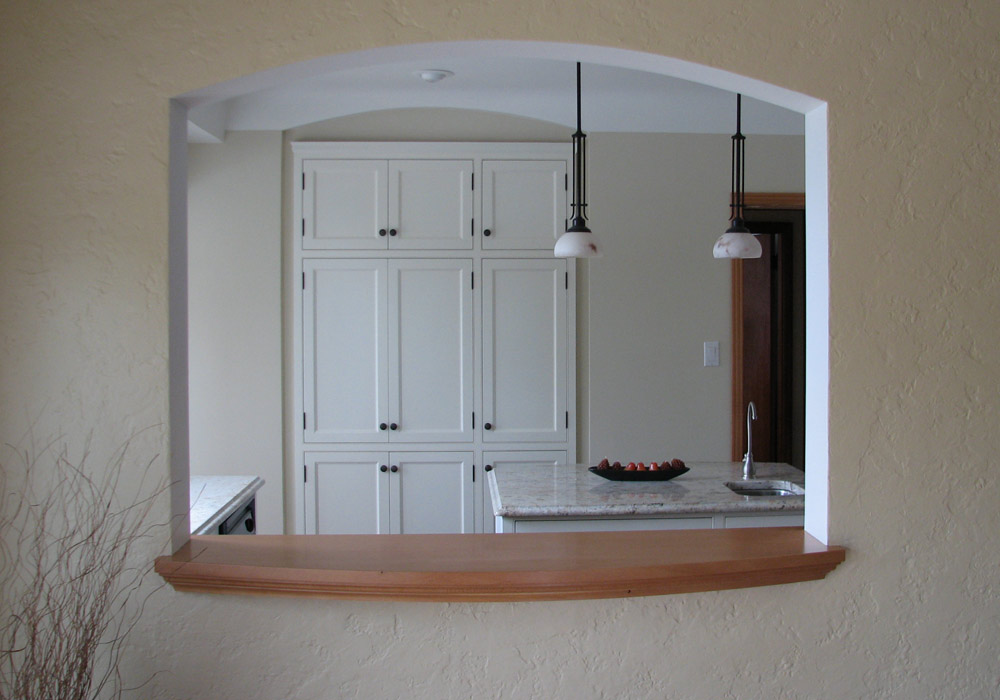 Face-frame kitchen viewed through arched opening, showing tall pantry cabinetry